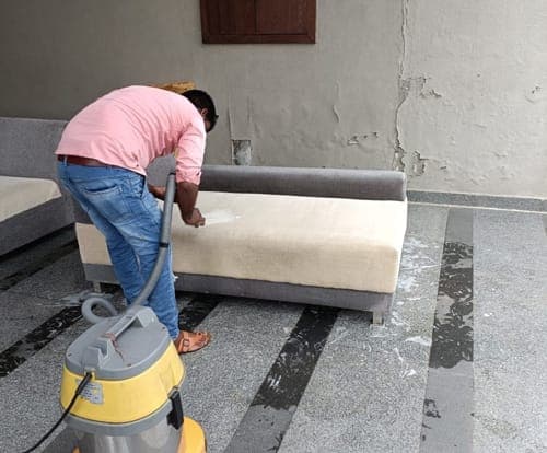 Team member cleaning a cream sofa seat with an extraction machine