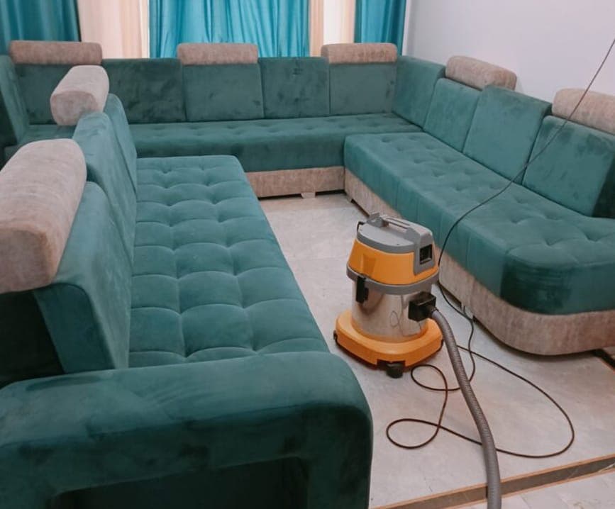 Green U-shaped sofa after cleaning, with a wet vacuum on the floor